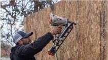 A man using a nailgun on a plywood wall