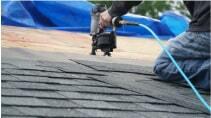 Photo of a person's side torso and leg kneeling on a roof and using a nailgun