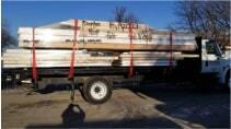 A large truck with several piles of flat sheets of building material strapped down on the bed of the truck