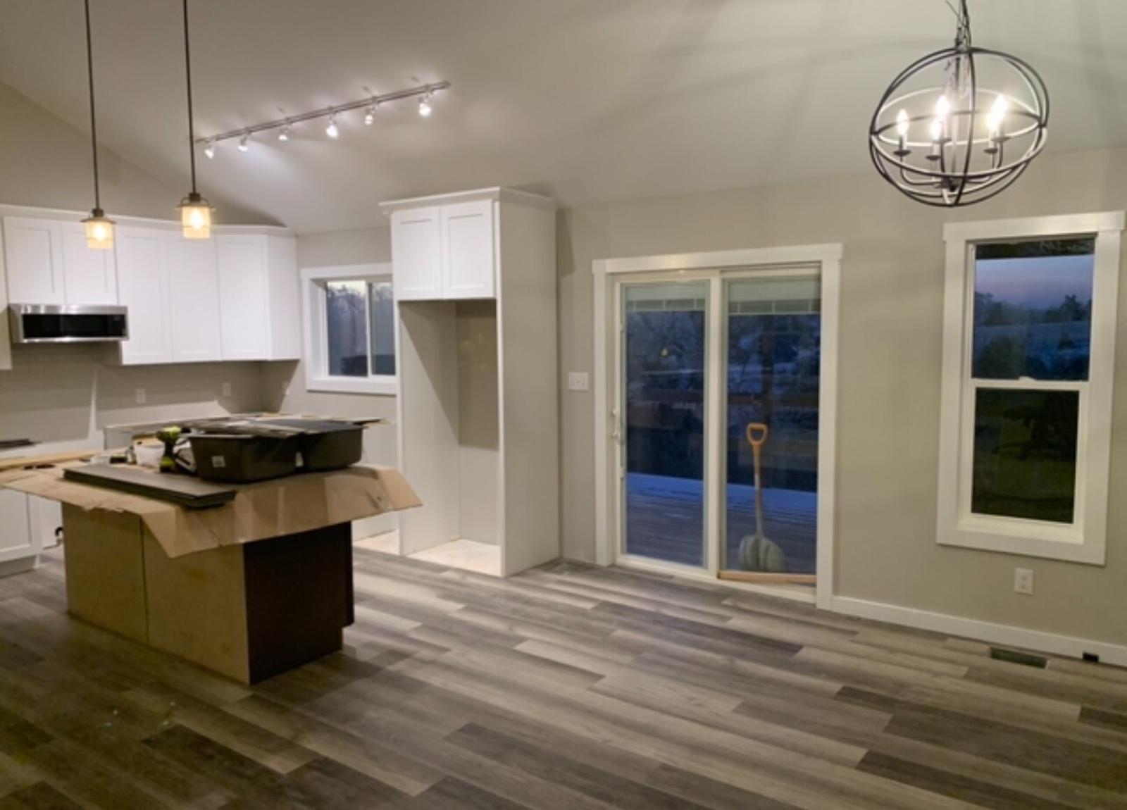 An interior view showing a partially finished kitchen and living room with track lighting and sliding doors leading to the porch.