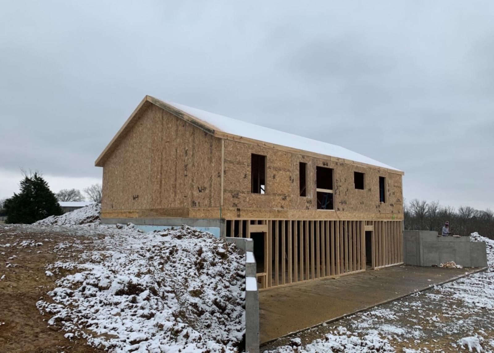 A house under construction with roof sheathing completed and basement framing visible.