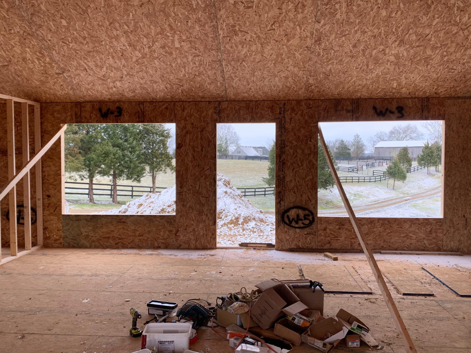 An interior view showing large window openings and a door under construction, with a view of the outside landscape.